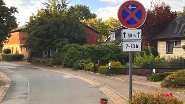 Das Bild zeigt den Bereich der Unterstraße, gegenüber der Grundschule in Oelixdorf. Darauf ein absolutes Halteverbotsschild mit der Kennzeichnung: 7-13 Uhr und geltend für den Bereich direkt gegenüber den Parkplätzen an der Grundschule.